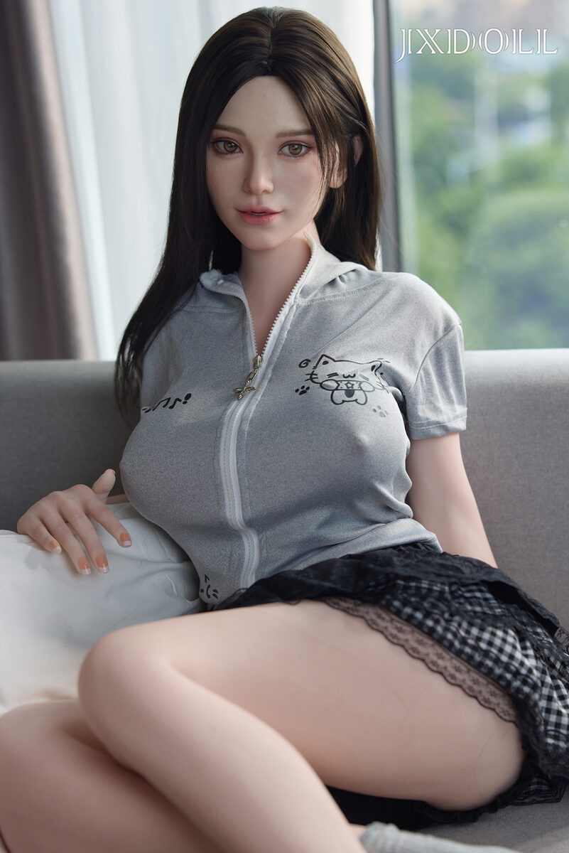 Sexpuppe Daisy im grauen Shirt und karierten Rock auf dem Sofa