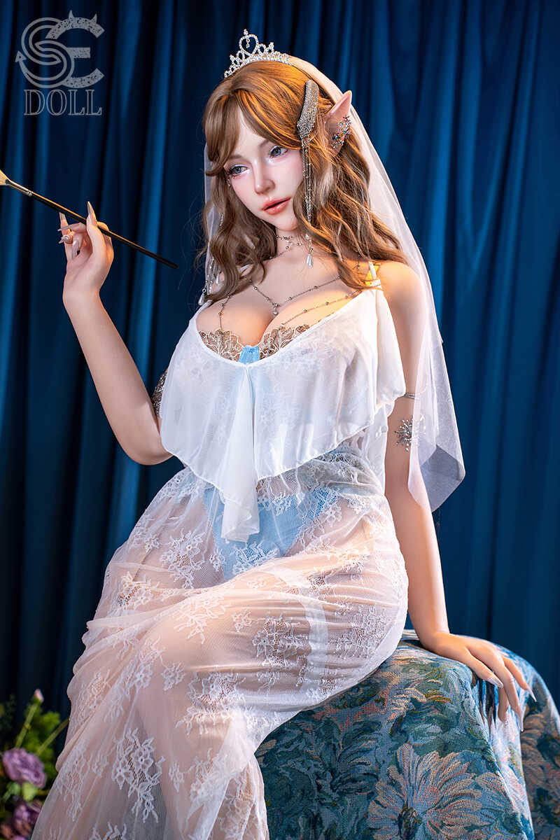 Real doll Annika.L in elegantem Spitzenkleid sitzend mit Pinsel und Staffelei
