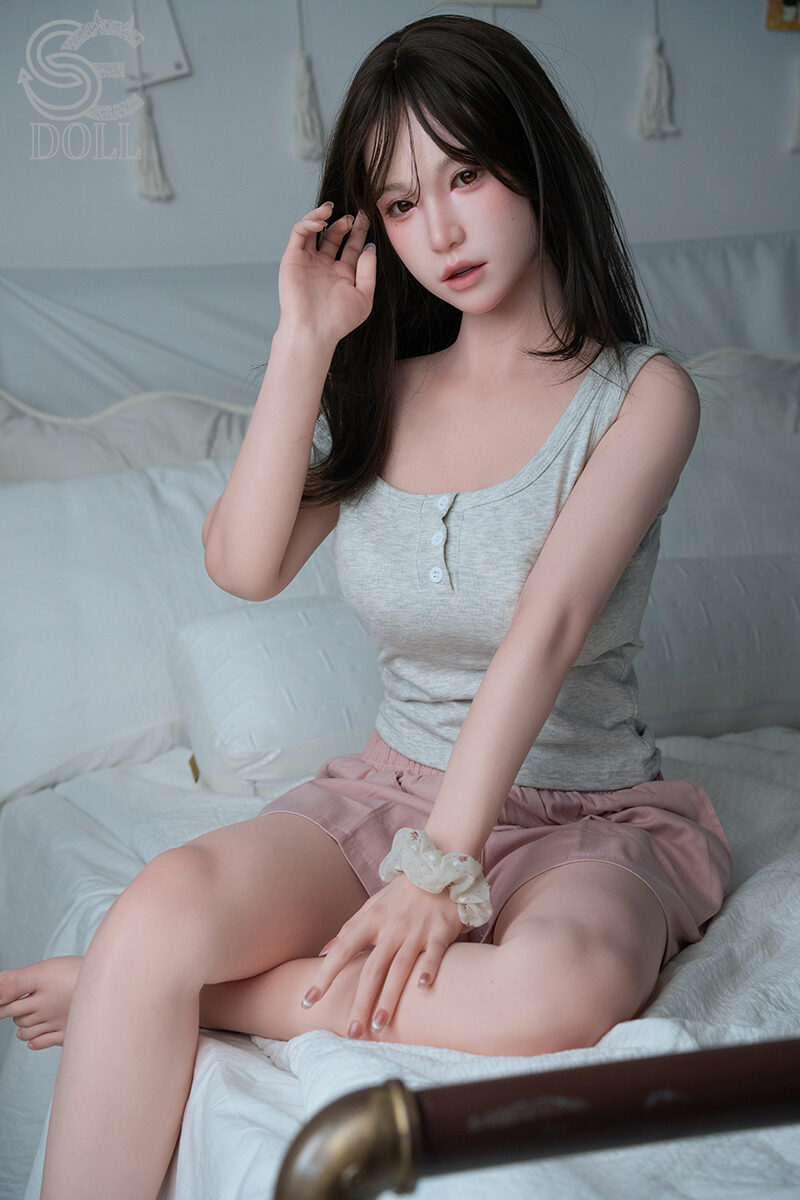 Real sexpuppe Sena.C im lässigen Outfit auf dem Bett sitzend